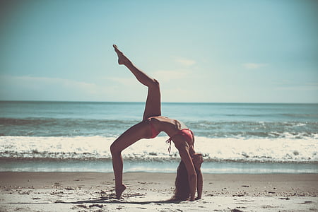woman in red bikini performing yoga near seashore