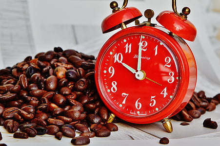 red and gold alarm clock beside coffee beans