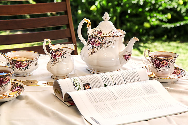 open magazine near white-and-pink floral tea set on top of table