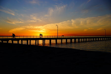 silhouette of couple walking on sea dock during golden hour