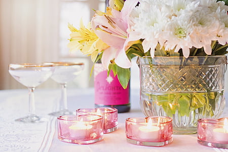 selective focus photography of tealight votive candles on table near floral arrangement and wineglasses