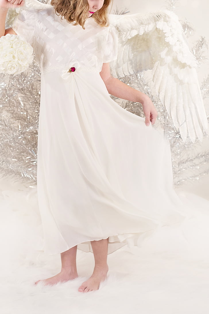 girl wearing white dress and wings standing on white rug