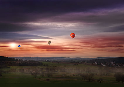 blue, yellow, and orange hot air balloons flying over green grass field during sunset