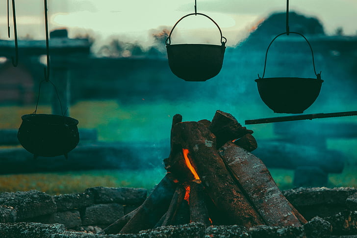 three pots hanged near campfire during dawn