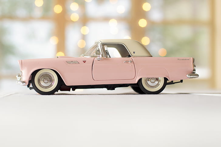 person taking photo of pink and white convertible coupe die-cast model