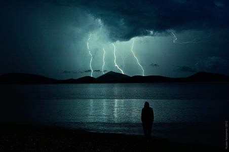 person standing near seashore and mountain cliff with thunder
