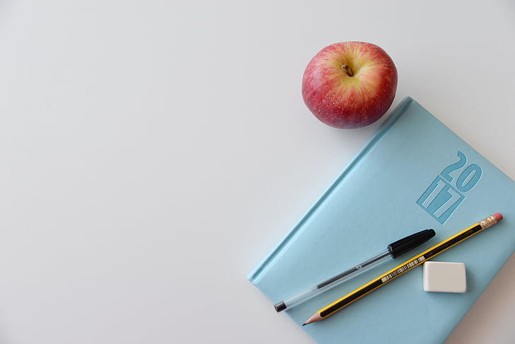 apple beside teal book and pencil