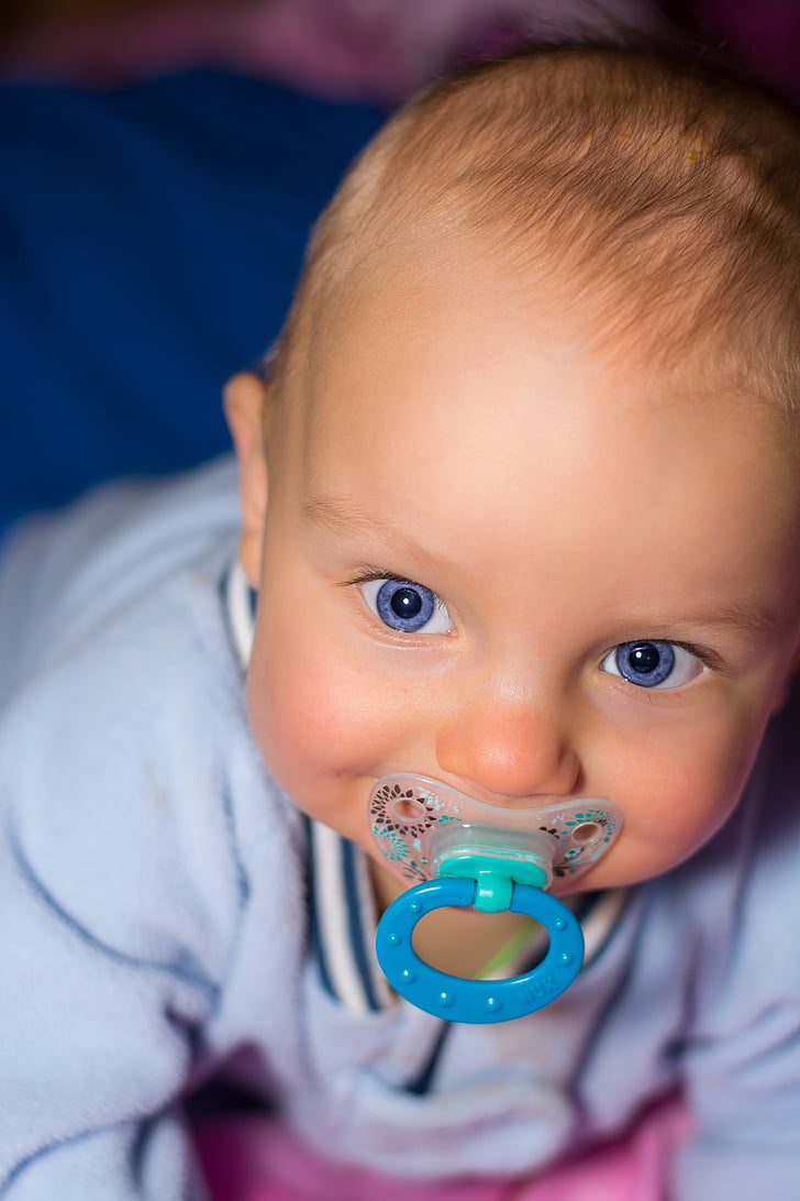 close up photo of baby biting blue pacifier
