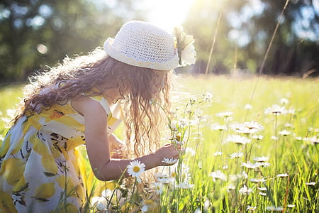 girl in yellow-white dress and white hat picking white petaled flowers