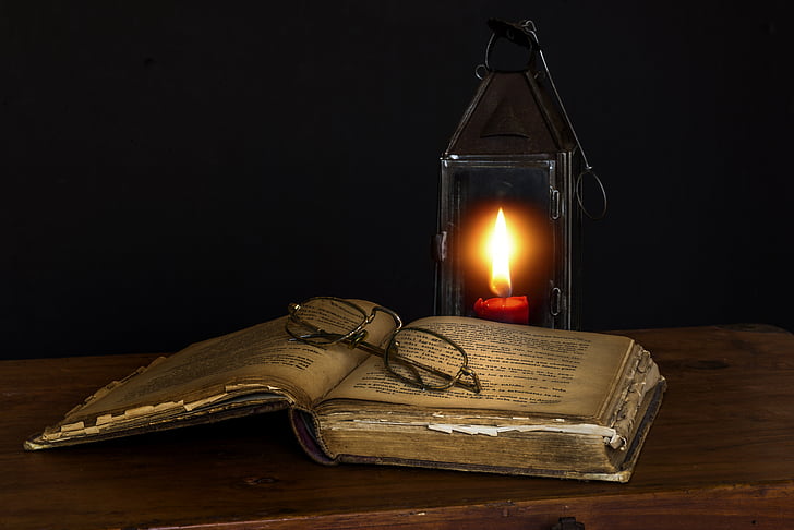 lighted candle near books and eyeglasses