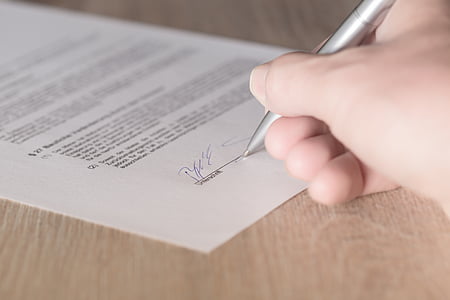 person holding pen while signing in printing paper
