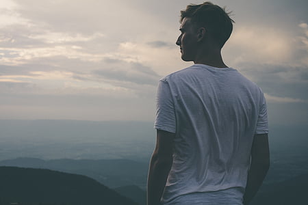 man wearing white t-shirt facing mountain landscape photo