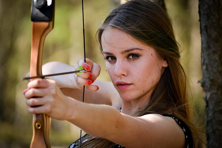 selective focus photography of woman in black top aiming her bow
