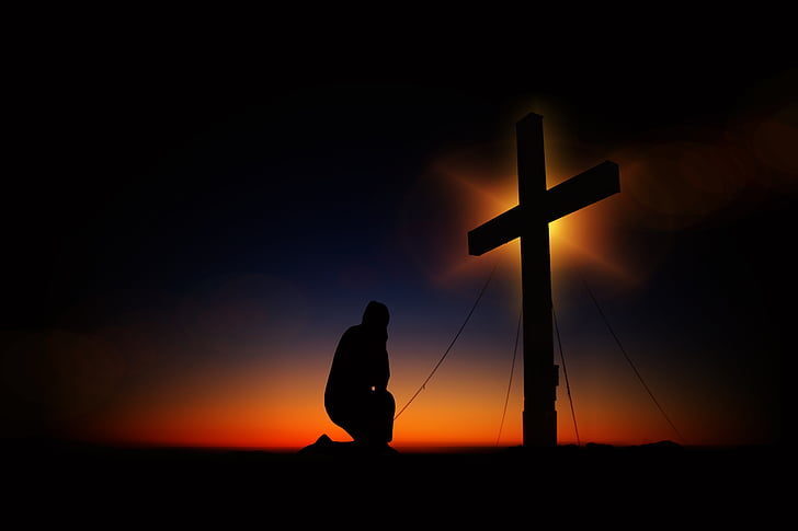 silhouette of man kneeling in front of a cross