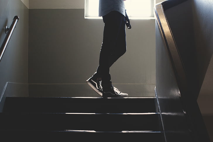 person wearing black skinny jeans and wearing black-and-white Vans sneakers standing on stair