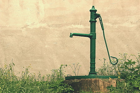 green hand pump surrounded by green grass