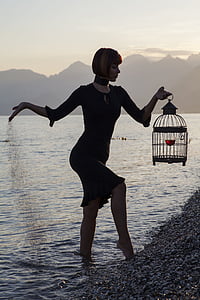 woman wearing black long-sleeved dress holding black metal birdcage