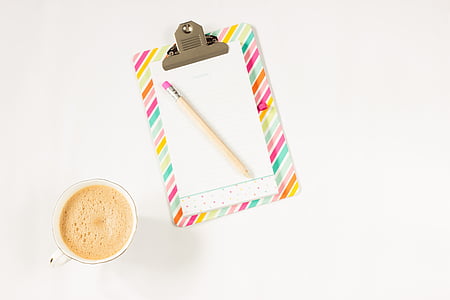 top-view photograph of clipboard, pencil, and cup filled with liquid