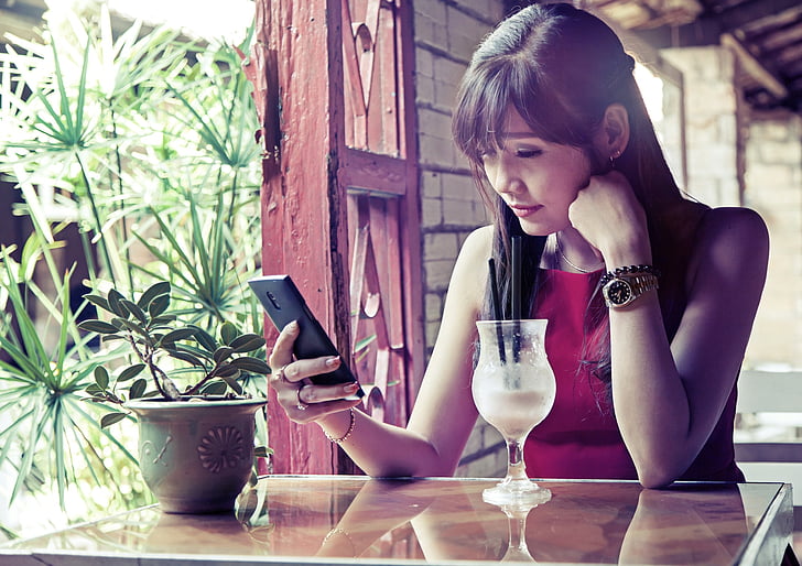 woman wearing red sleeveless top using smartphone while sitting near table