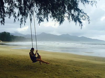 woman sitting on swing attached on tree on seashore