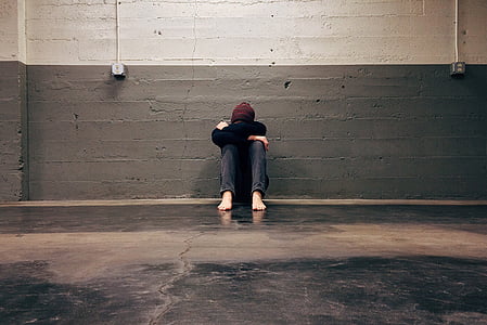 person sitting on floor leaning on gray concrete wall