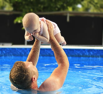 father lifting baby on pool during faytime