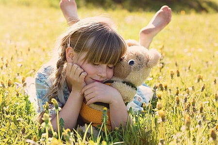 girl with brown bear push toy smiling white lying on grass field