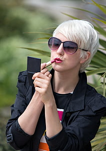 woman wearing black collared shirt putting red lipstick during daytime