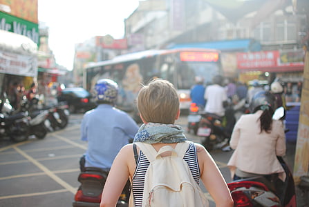 woman facing back with beige backpack standing beside motorcycle