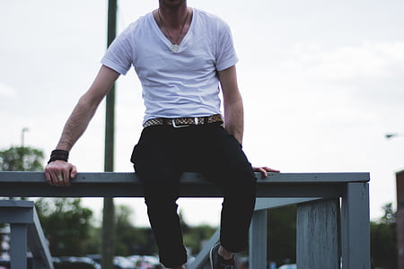 man in white shirt and black pants sitting on gray fence