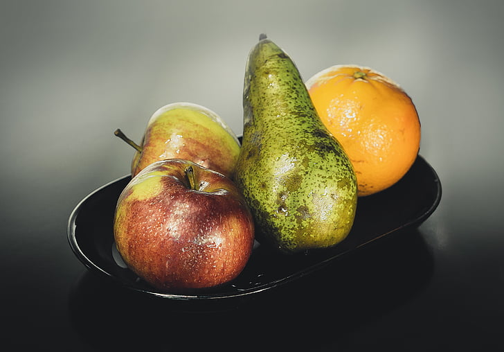 two apples, avocado, and orange on black ceramic plate