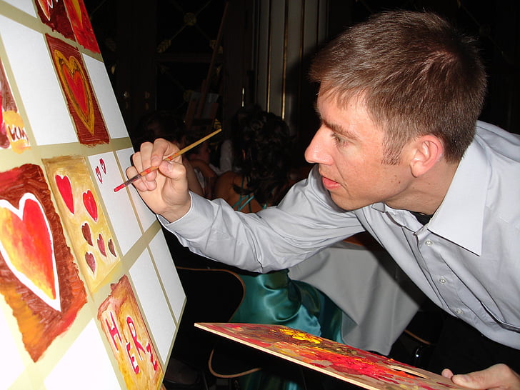 man painting brown and red hearts on white canvas