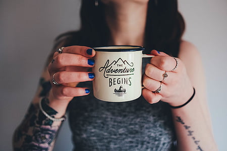 closeup photography of person holding white the adventure begins printed mug