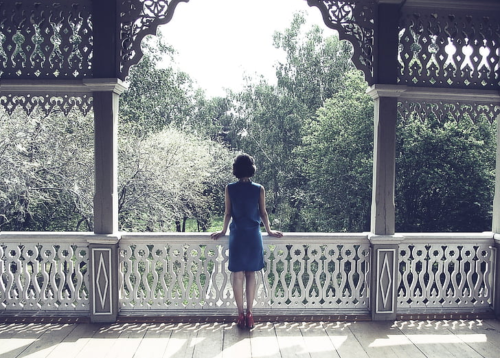 woman standing on balcony while facing trees