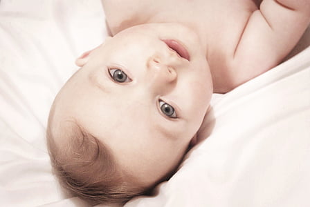 baby lying on white textile