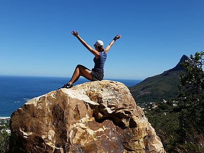woman wearing blue tank top sitting in top of rock with a view of sea