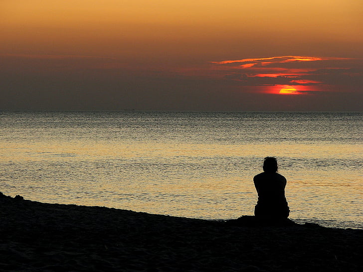 person sitting near seashore during golden hour