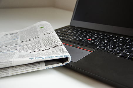 newspaper beside black Lenovo thinkpad
