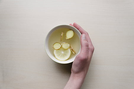 person holding white ceramic cup with sliced ginger and lemon