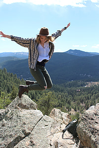 photo of woman jumping beside cliff during daytime