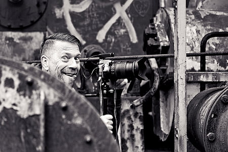 grayscale photo of man smiling in front of DSLR camera