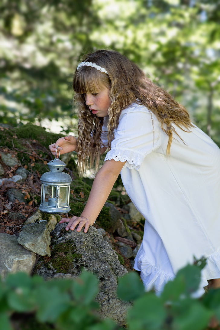 shallow focus photography of girl wearing white dress holding silver-colored kerosene lamp on her right hand during daytime