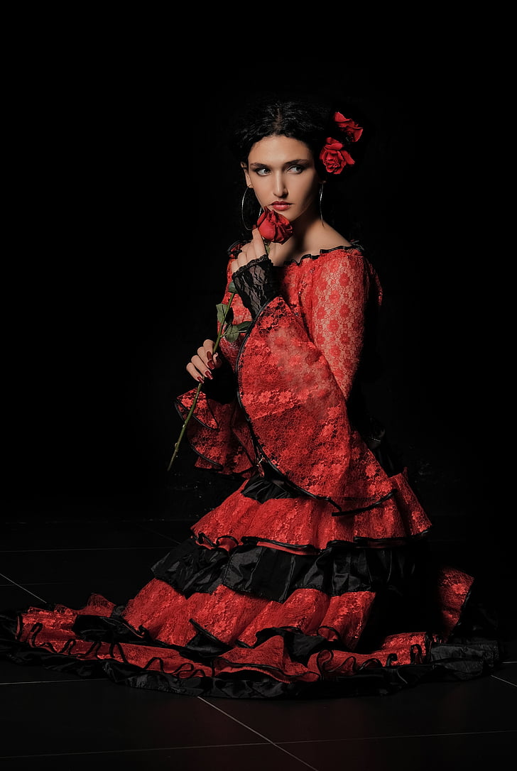 woman wearing red and black long-sleeved ruffled dress holding rose on black background