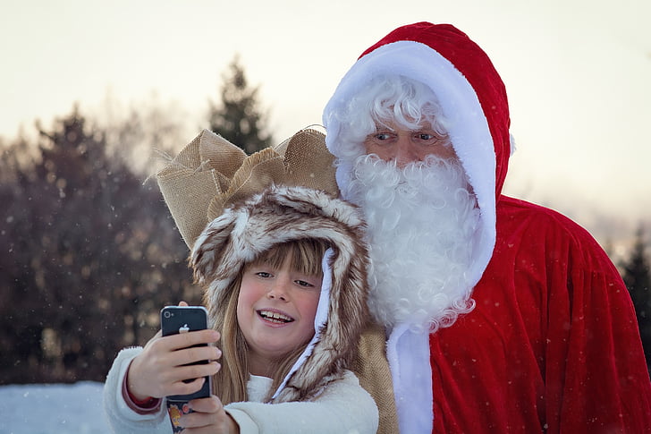 child taking selfie next to man in Santa Claus costume