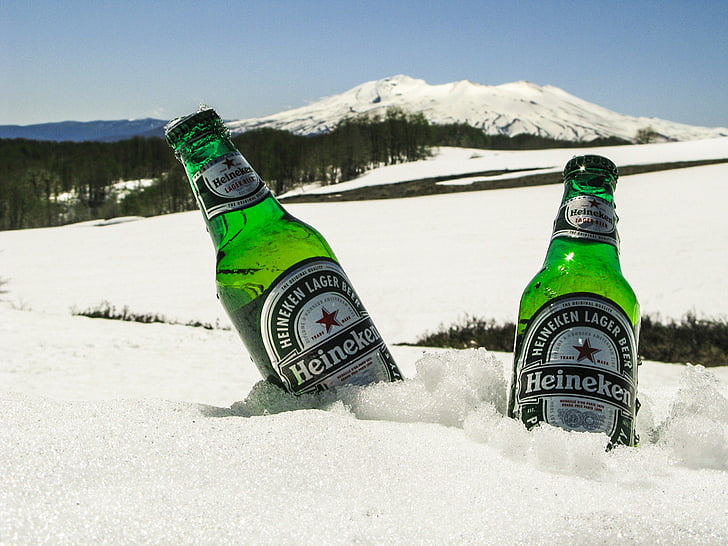 two Heineken beer bottles in snow field far away snow mountain
