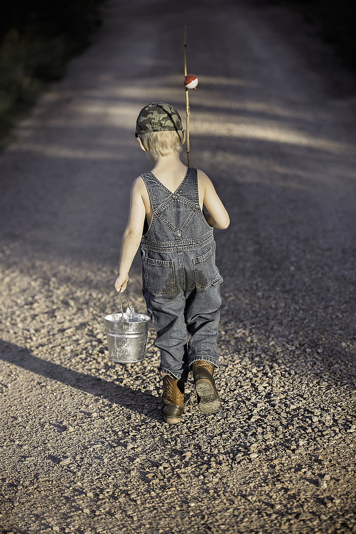 boy in blue denim overalls holding metal bucket and fishing rod