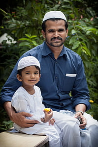 man in blue dress shirt sitting beside toddler in white thobe