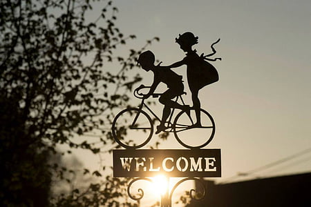 silhouette of two children on bike with welcome sign