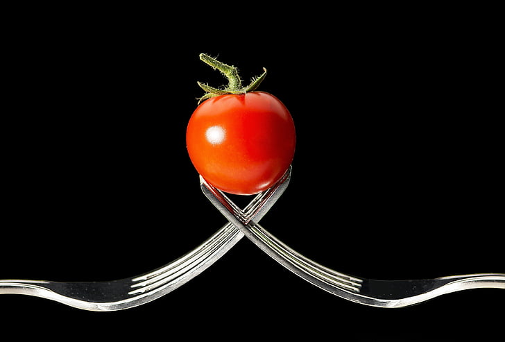 photo of tomato between the tips of two forks