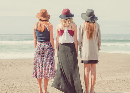 three women standing at the beach looking at the ocean during day